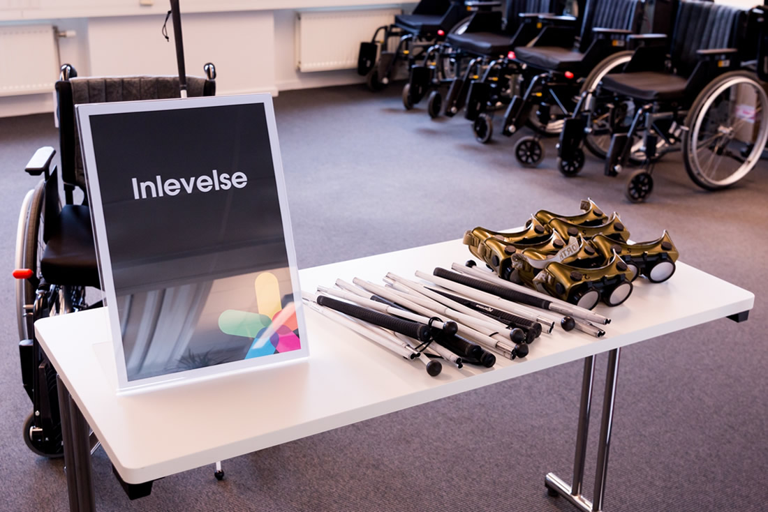 A table with impairment glasses and folded white canes and a sign in Swedish announcing empathy exercises. In the background, a row of wheelchairs.