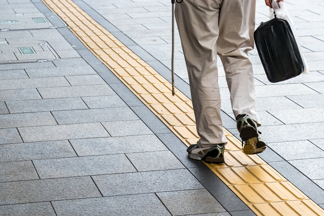 A person with white cane walk and use tactile marking and colour contrast on the street to navigate. Photo