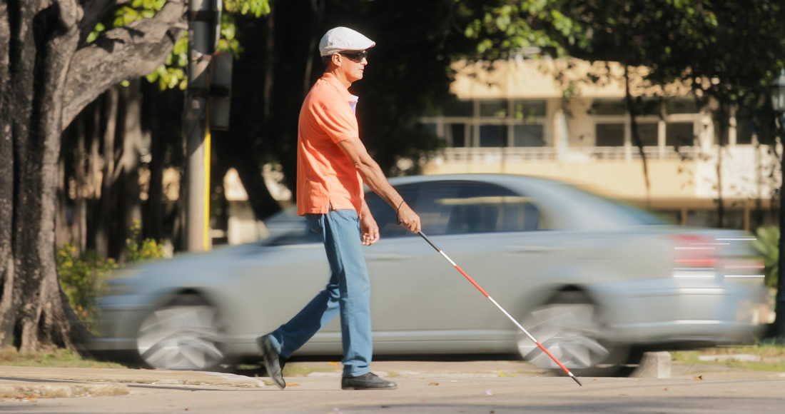 A blind person walk near a car and the traffic. Photo