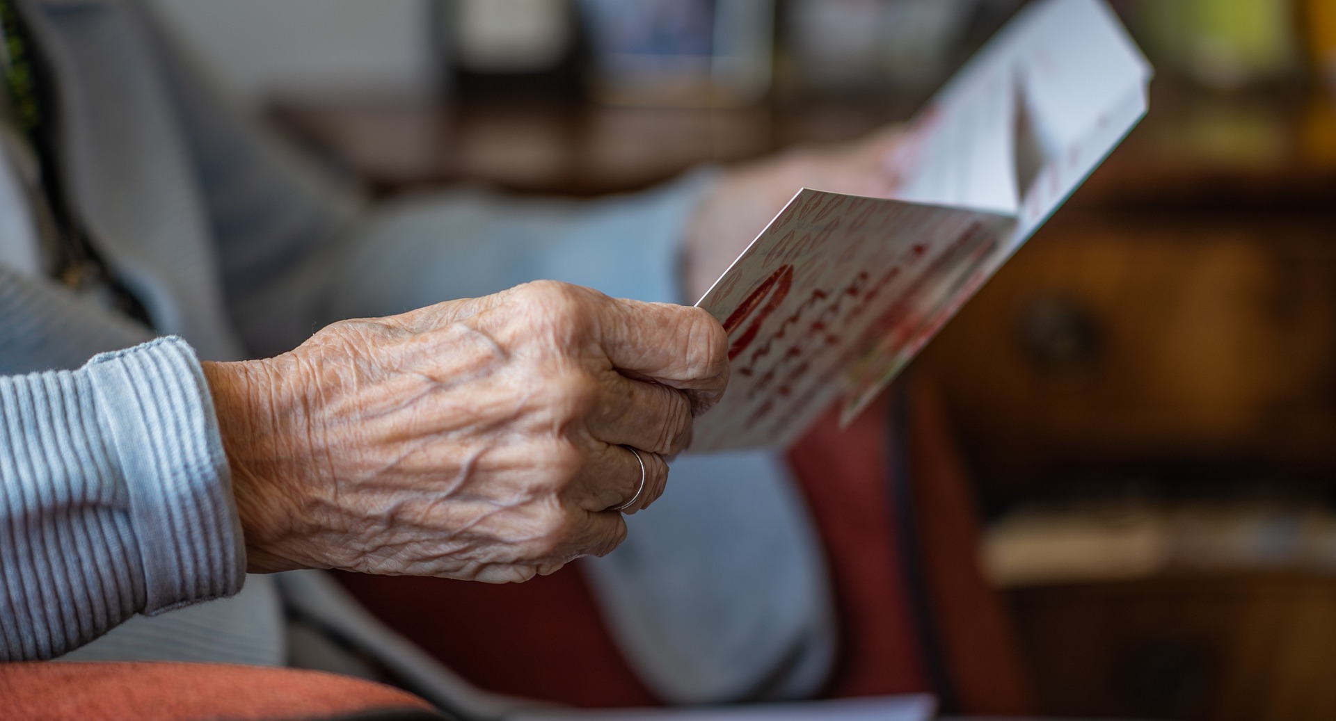 Detail rúk seniorky, ktorá má v rukách pozdrav alebo kartičku.