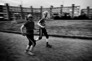 ČB fotografia, dvaja bežci, muž a žena bežia po ceste, v pozadí vidno rozmazané paneláky.