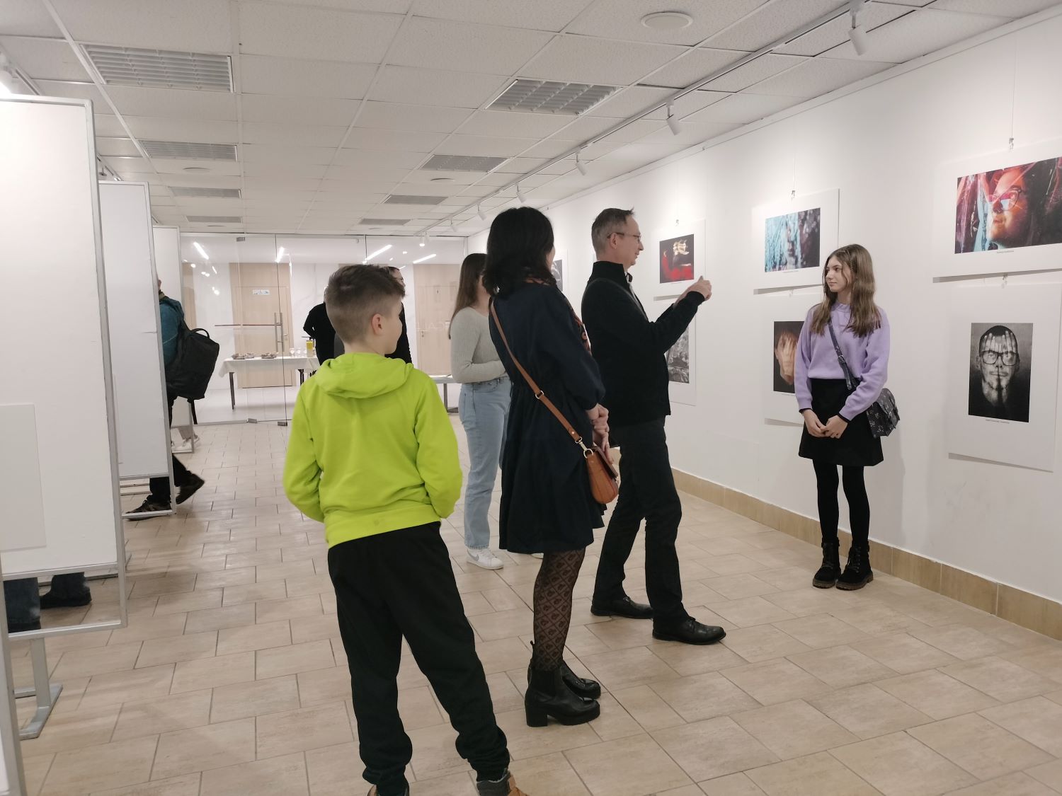 Pred fotografiou stojí slečna, fotí ju otec a zvyšní ľudia - návštevníci sa prizerajú.