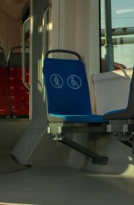 Na obrázku je záber na sedačku v autobuse, ktorá je modrej farby a na chrbtovej časti má výrazné biele piktogramy s označením človeka s bielou palicou či nastávajúcej matky.
