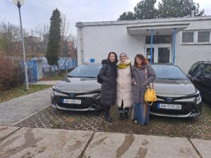 Pred autami stoja T. Winterová, S. Tóthová a Z. Egydová. Autá sú už odparkované na parkovisku ÚNSS. 