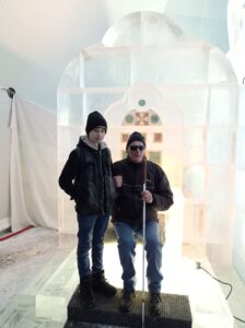 Na obrázku je nevidiaci muž s bielou palicou a pri ňom chlapec. Stoja v ľadovej sieni.