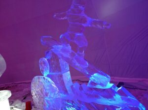 Na obrázku je športovec - snowboardista vytvorený iba z ľadu a farebne podsvietený (fialovo-modro).