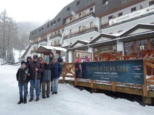 Skupina nevidiacich i vidiacich turistov pred budovou hotela, stoja na chodníku plnom snehu. 