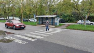 Na priechode pre chodcov ide muž s bielou palicou. Pred priechodom stojí a čaká červené osobné auto.