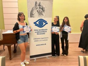Pri banneri ÚNSS stoja usmiate žiačky s diplomami.