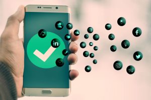 Na obrázku je ruka držiaca mobil, na ňom je veľký znak "fajočka" ako potvrdené/schválené a z mobilu vychádzajú bublinky, na ktorých sú ikonky rôznych aplikácií.